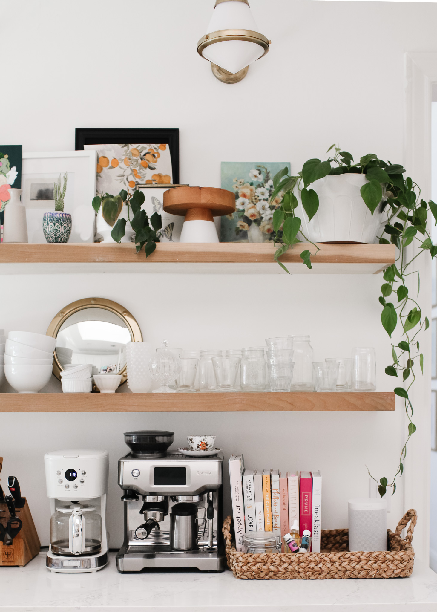 open kitchen shelving with glasses, plants and art. espresso machine and coffee maker on counter