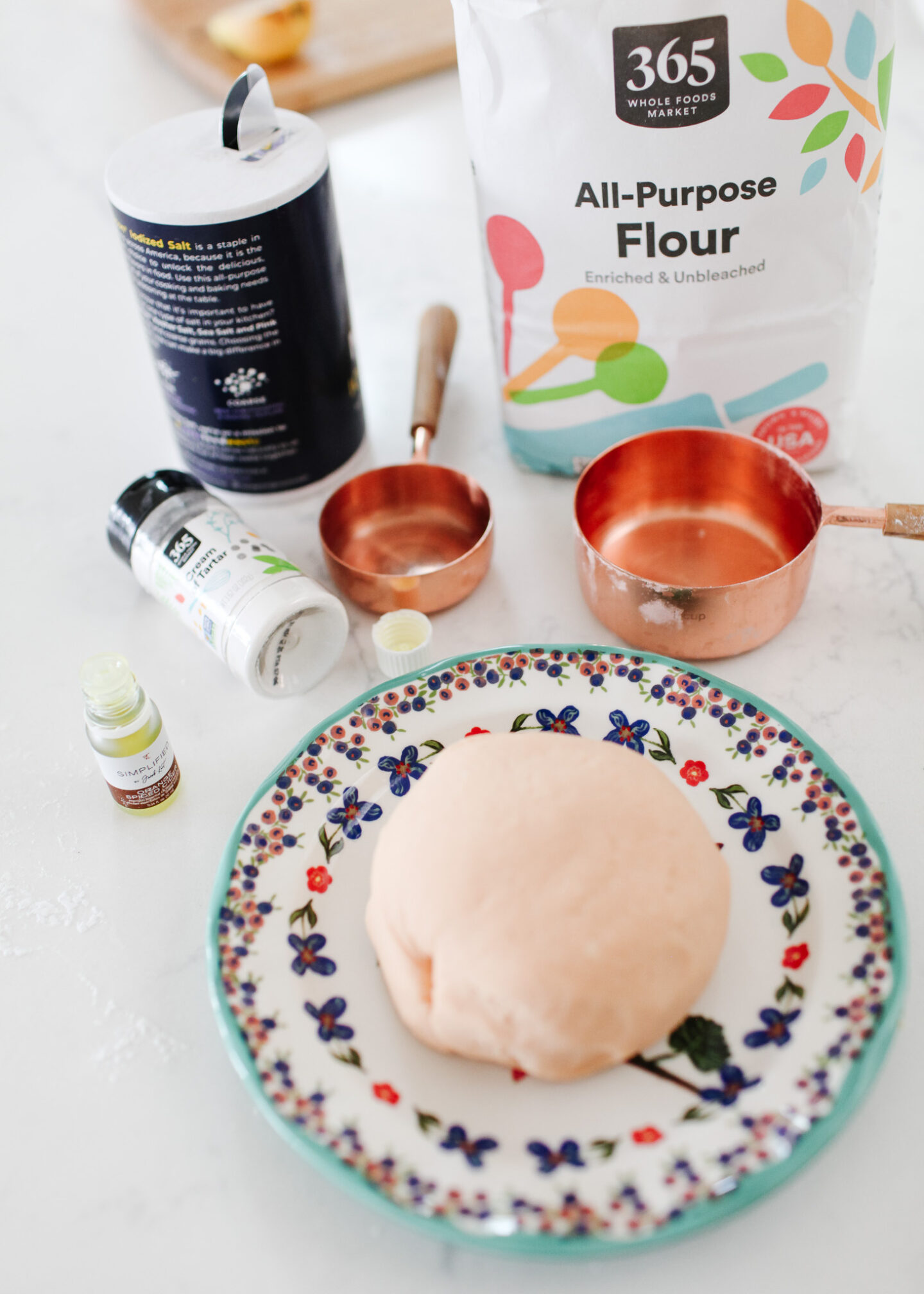 Homemade playdough on plate with ingredients and measuring cups around it.