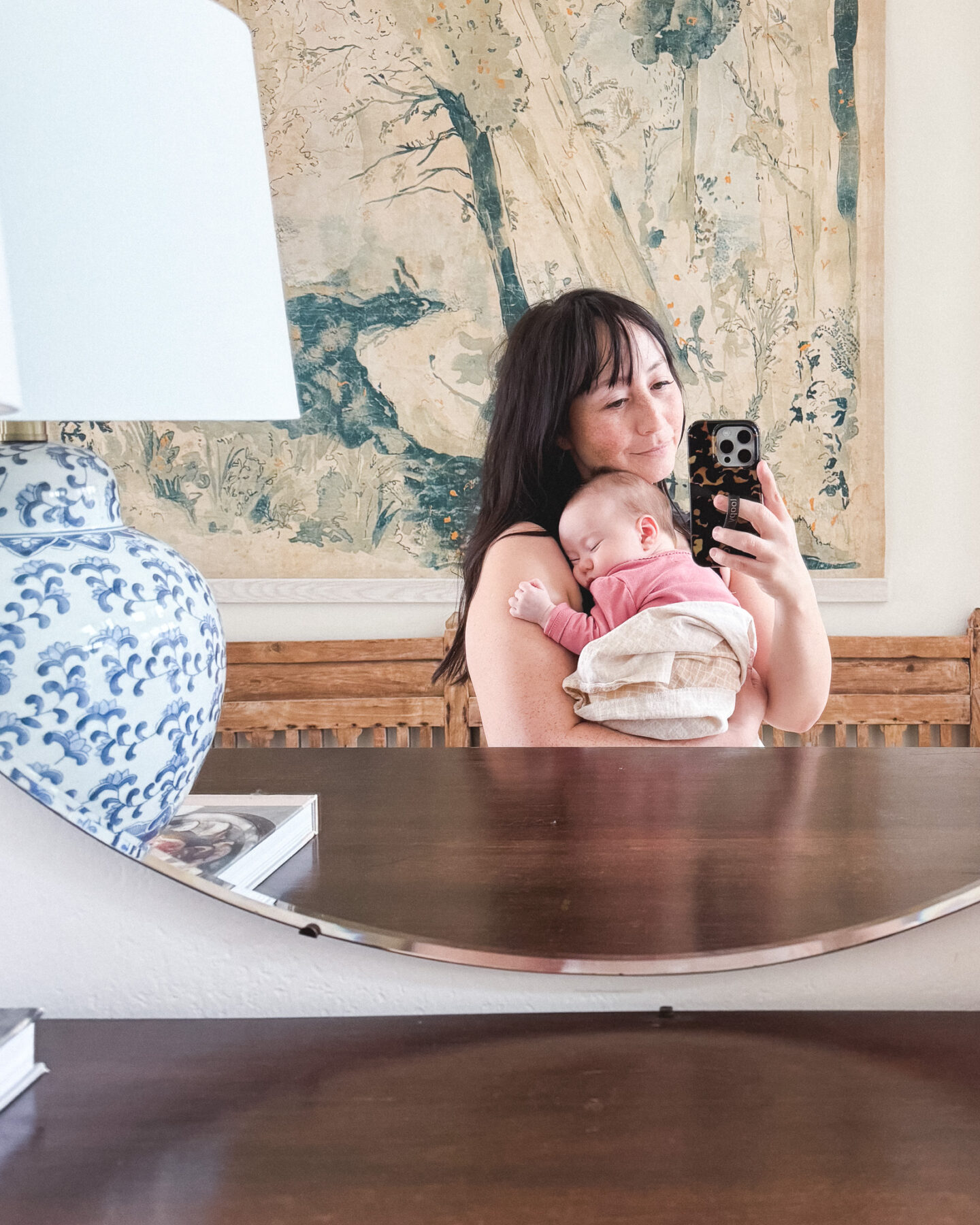 Mother holding baby in front of mirror with cell phone