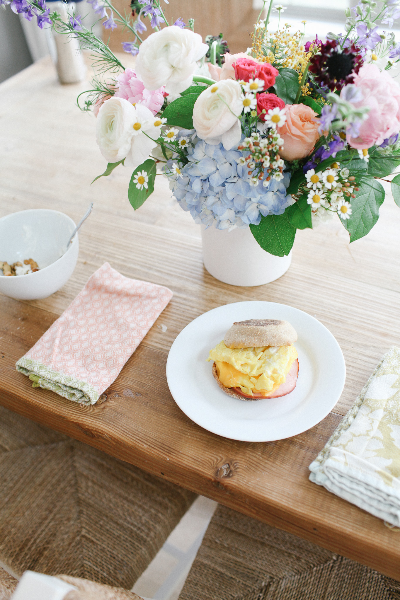 breakfast sandwiches and flowers on dining table with cloth napkins
