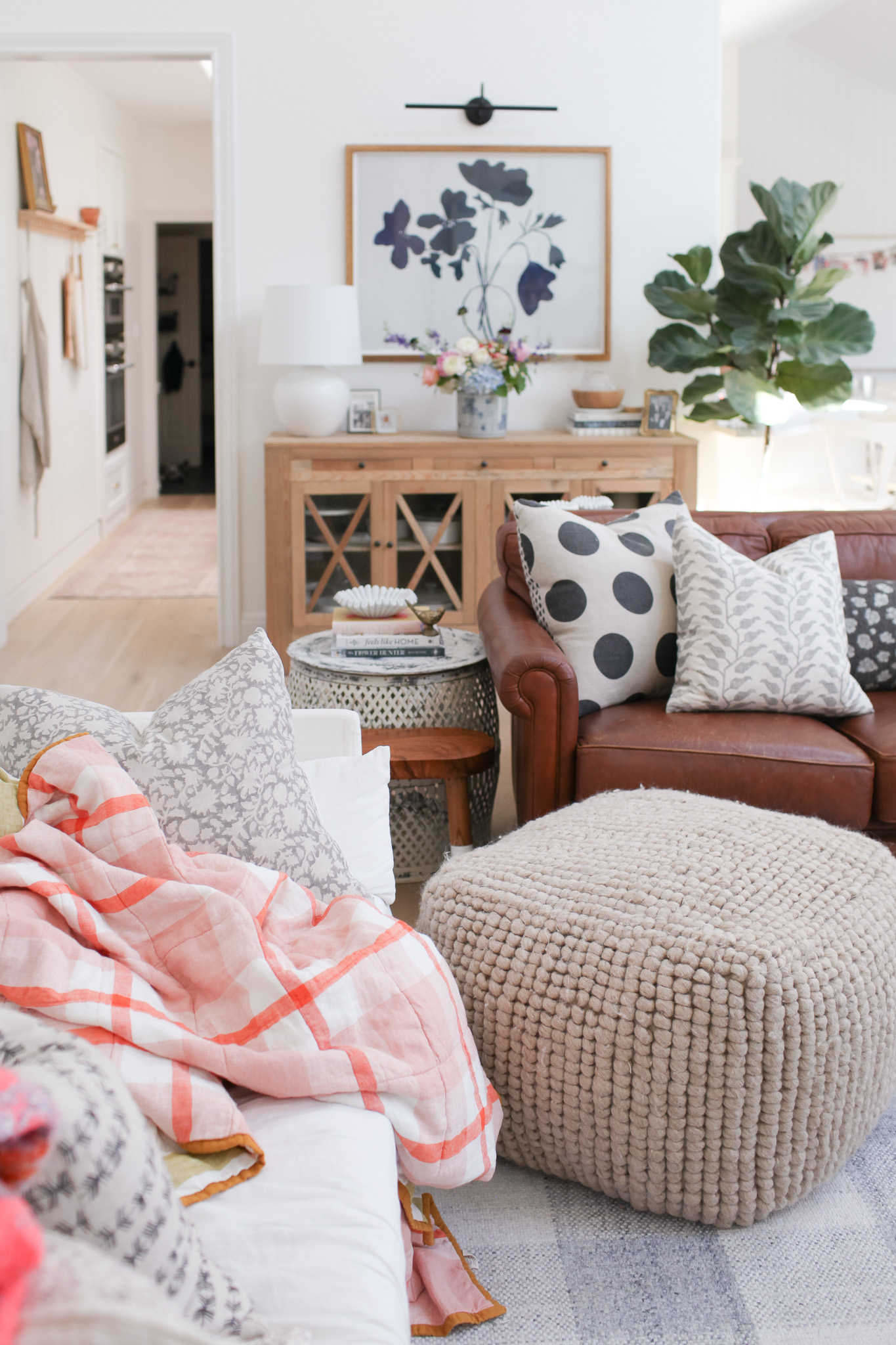 living room with black and white floral art, 2 sofas and a pouf. Pink plaid quilt.