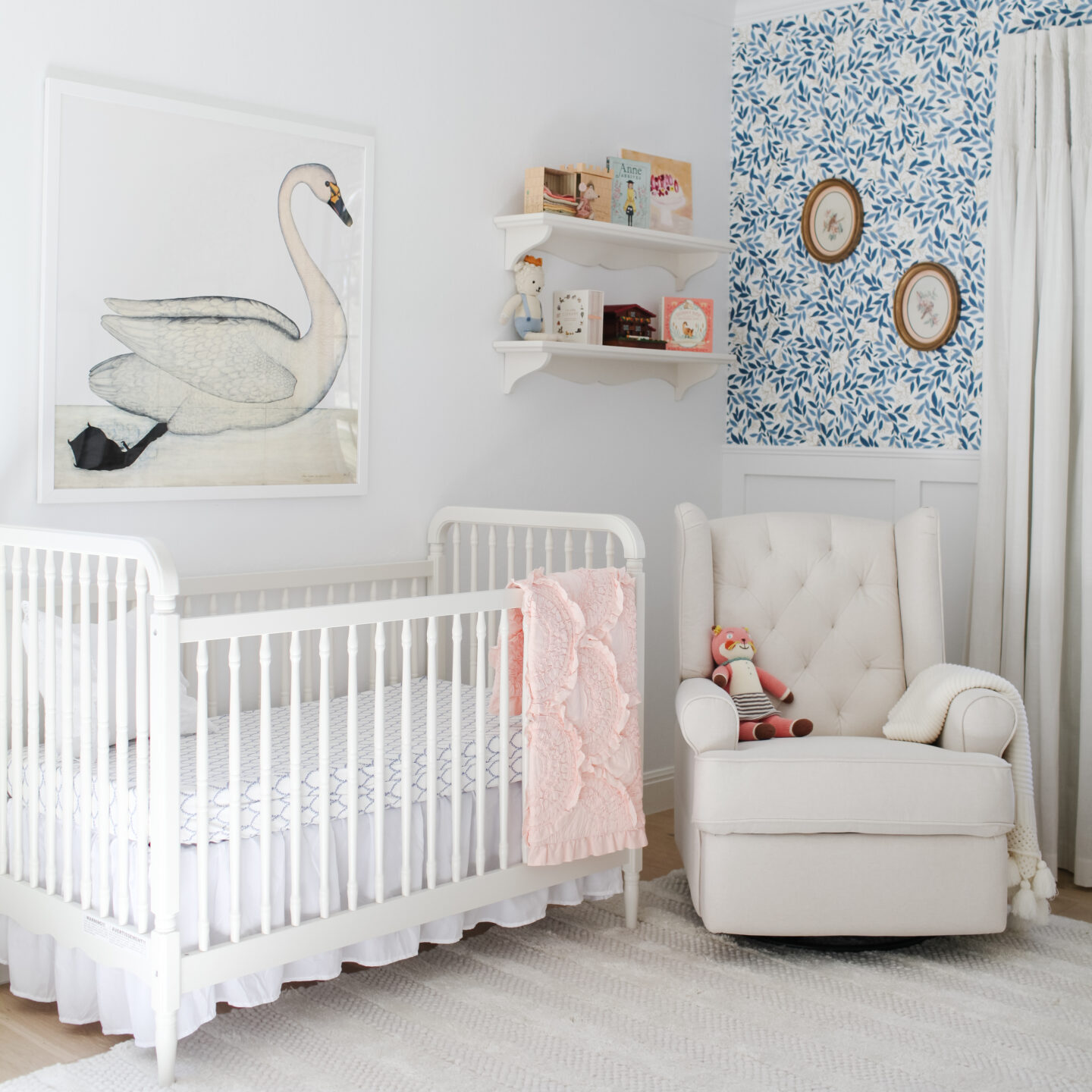 Wide shot of baby girl nursery with crib, and reclining glider. Vintage oval floral art from Etsy, large swan framed art over crib.